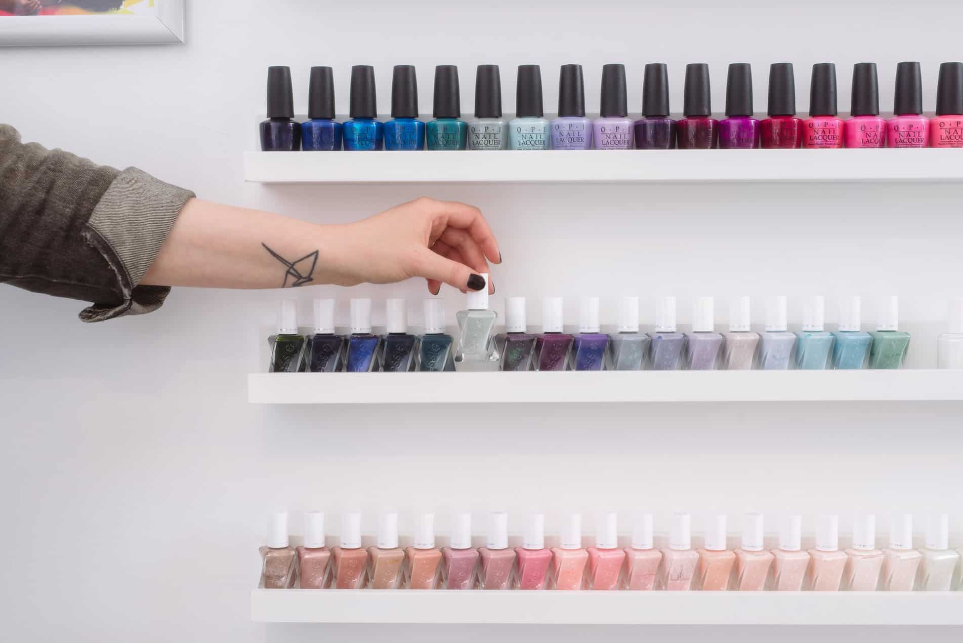 wall of nail polish with a person picking a grey color