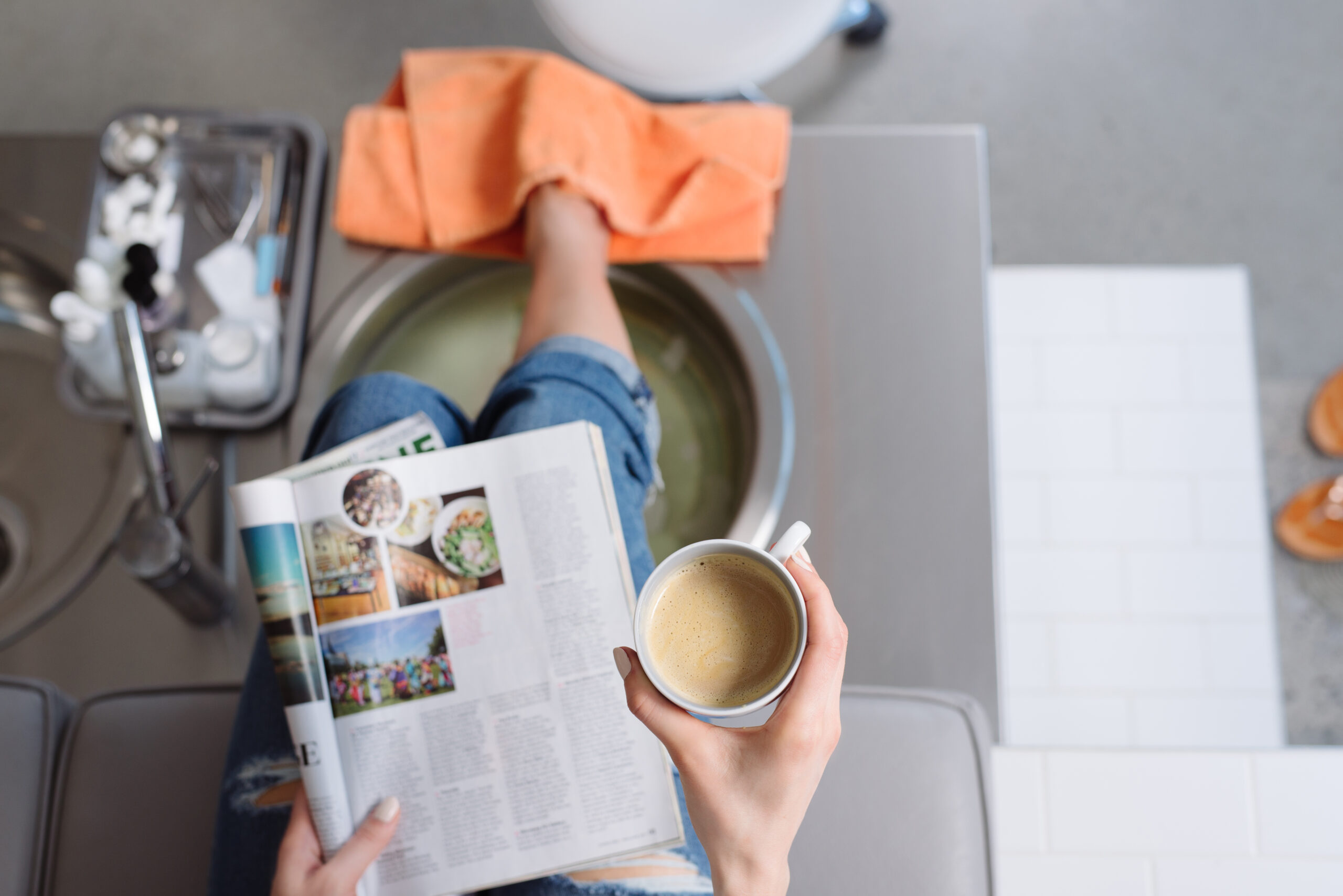 woman getting a pedicure while holding a cup of coffee and reading a newspaper